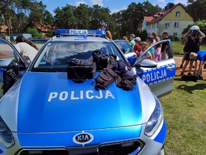 Policyjny radiowóz i wyposażenie, w tle dzieci i policjant