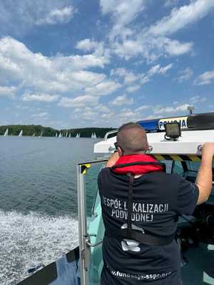 Na policyjnej łodzi stoi mężczyzna ze specjalistycznej grupy