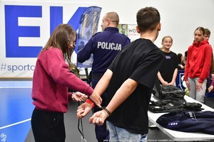 Policjant pokazuje uczniom na hali wyposażenie Policyjne