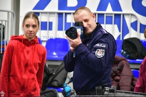 Policjant pokazuje uczniom na hali wyposażenie Policyjne