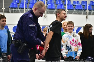 Policjant pokazuje uczniom na hali wyposażenie Policyjne