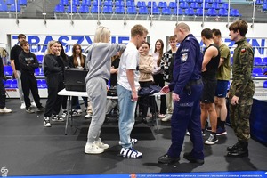 Policjant pokazuje uczniom na hali wyposażenie Policyjne