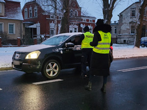 Policjant w towarzystwie pracownicy socjalnej kontrolujący kierowce pojazdu.