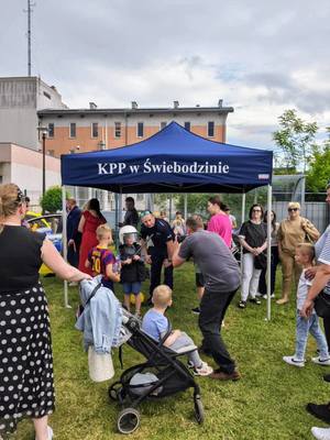 Policyjne stoisko, namiot, ludzie, mierzenie prędkości w biegu, przymierzanie strojów, dzieci uśmiechnięte w radiowozie.