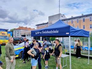 Policyjne stoisko, namiot, ludzie, mierzenie prędkości w biegu, przymierzanie strojów, dzieci uśmiechnięte w radiowozie.
