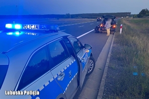 radiowóz, w tle policjant wymienia koło w aucie