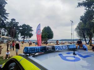 Radiowóz, pojazd ratowników i plaża z ludźmi w tle
