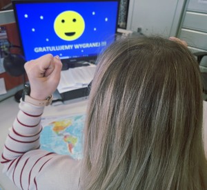 kobieta unosząca ręce w geście zwycięstwa a w tle komputer z napisem gratulujemy wygranej