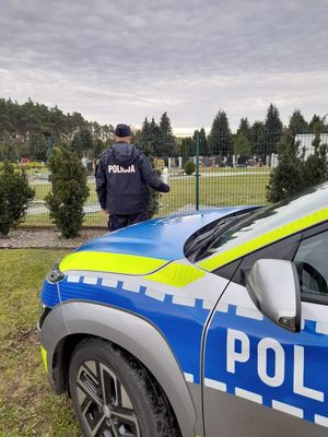 Policjant przy radiowozie ze zniczem, znicz przy nagrobku