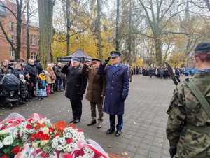 Policjant, strażak i leśnik składają kwiaty pod pomnikiem