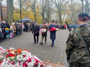 Policjant, strażak i leśnik składają kwiaty pod pomnikiem