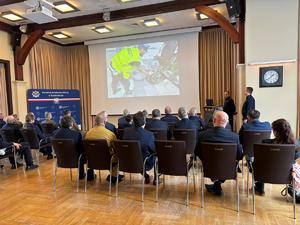 Zdjęcia z odprawy, sala, wyświetlona prezentacja, przemówienia i mundurowi oraz goście na krzesłach